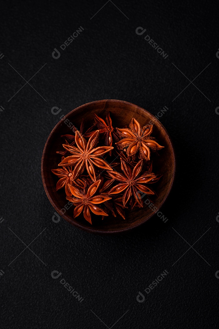 Anis estrelado em forma de estrela em uma tigela redonda de madeira sobre um fundo escuro de concreto