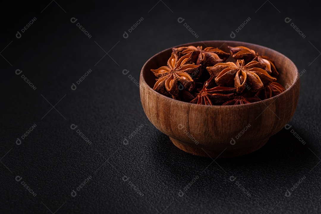 Anis estrelado em forma de estrela em uma tigela redonda de madeira sobre um fundo escuro de concreto