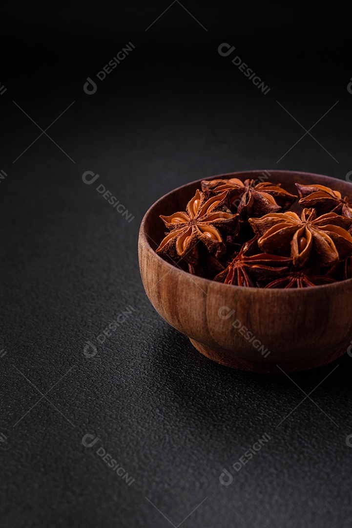 Anis estrelado em forma de estrela em uma tigela redonda de madeira sobre um fundo escuro de concreto