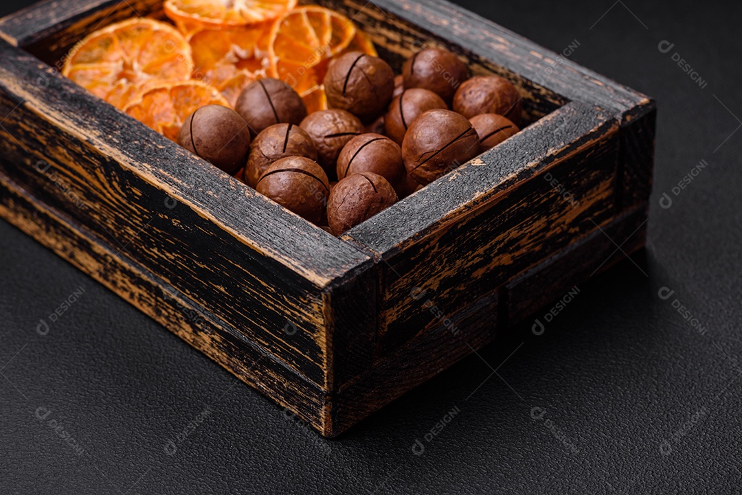 Deliciosas nozes de macadâmia torradas com casca sobre um fundo de concreto texturizado escuro. Comida vegetariana