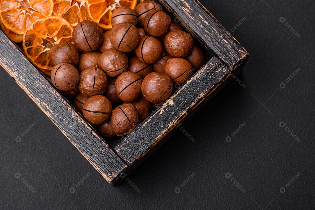 Deliciosas nozes de macadâmia torradas com casca sobre um fundo de concreto texturizado escuro. Comida vegetariana