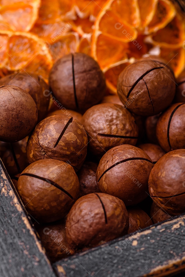 Deliciosas nozes de macadâmia torradas com casca sobre um fundo de concreto texturizado escuro. Comida vegetariana