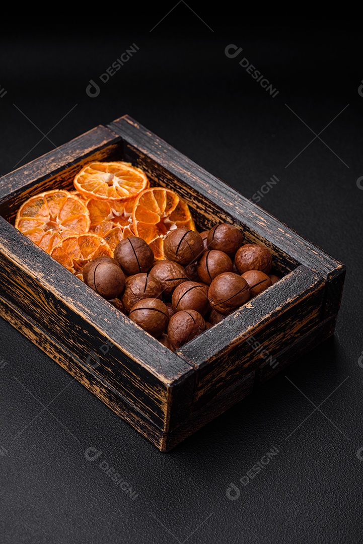 Deliciosas nozes de macadâmia torradas com casca sobre um fundo de concreto texturizado escuro. Comida vegetariana