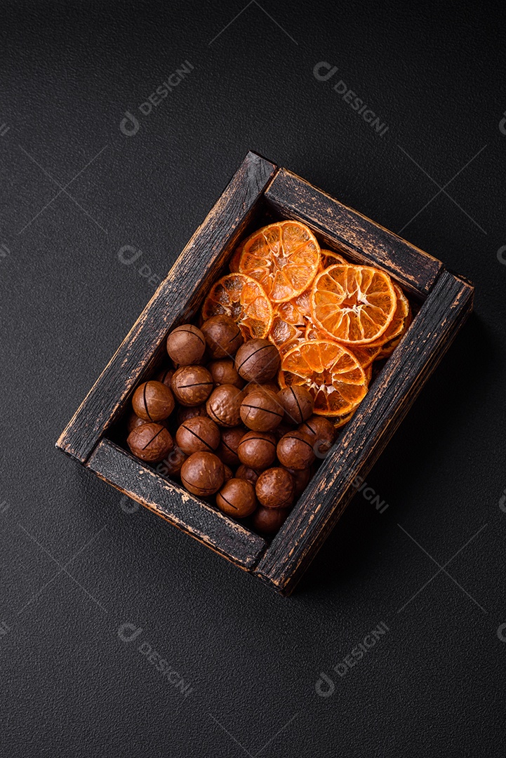 Nozes torradas e nozes de macadâmia, tangerina seca, frutos secos sobre um fundo escuro de concreto