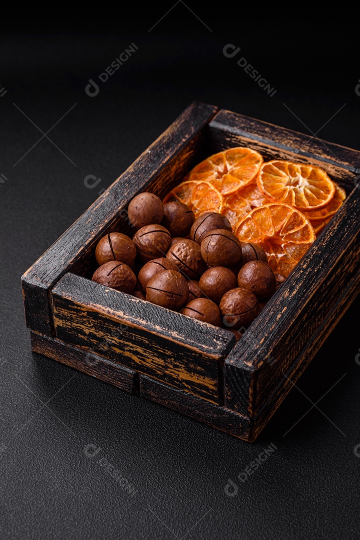 Nozes torradas e nozes de macadâmia, tangerina seca, frutos secos sobre um fundo escuro de concreto