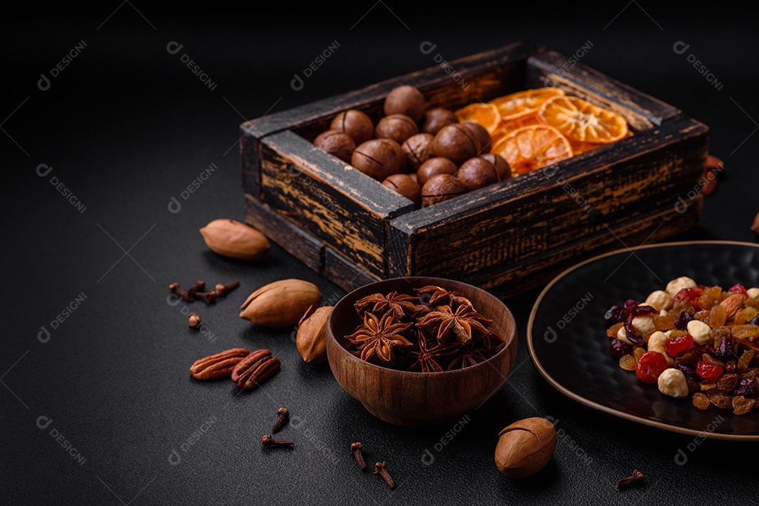 Nozes torradas e nozes de macadâmia, tangerina seca, frutos secos sobre um fundo escuro de concreto