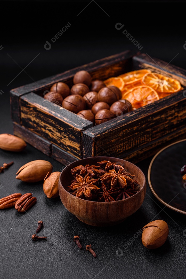 Nozes torradas e nozes de macadâmia, tangerina seca, frutos secos sobre um fundo escuro de concreto