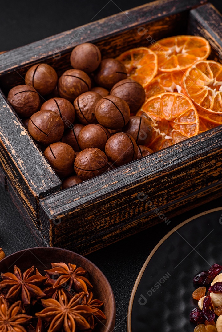 Nozes torradas e nozes de macadâmia, tangerina seca, frutos secos sobre um fundo escuro de concreto