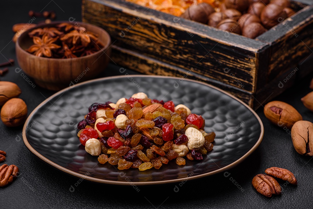 Nozes torradas e nozes de macadâmia, tangerina seca, frutos secos sobre um fundo escuro de concreto