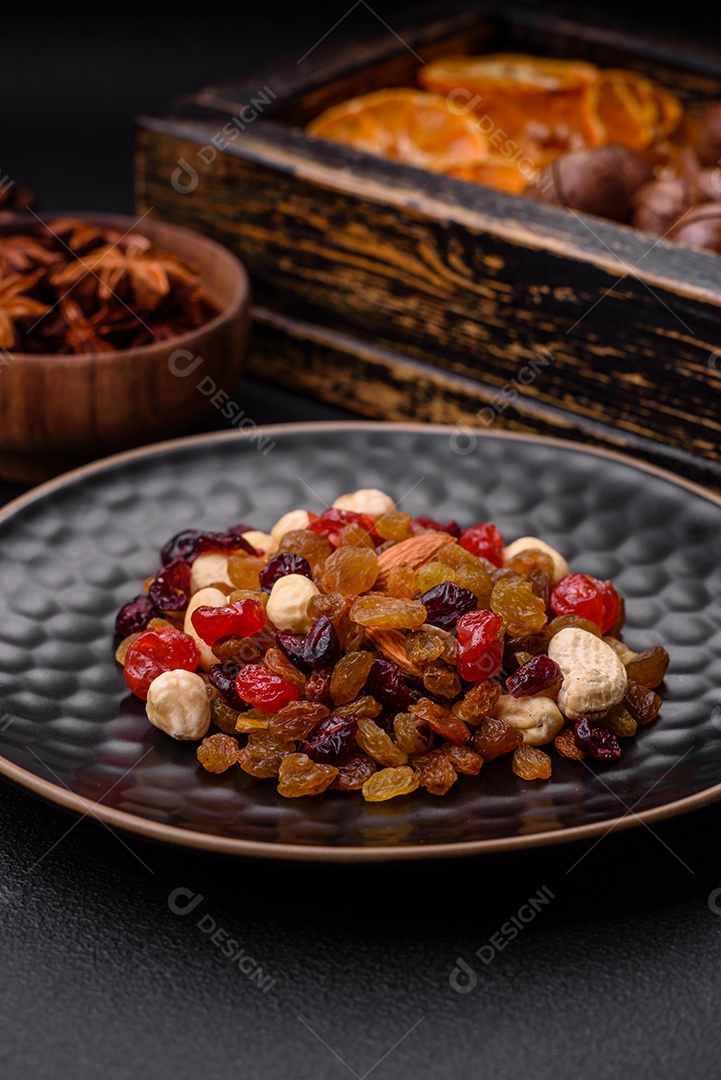 Nozes torradas e nozes de macadâmia, tangerina seca, frutos secos sobre um fundo escuro de concreto