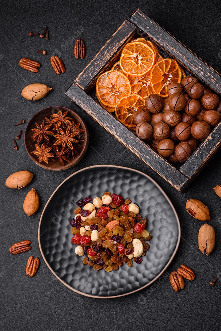 Nozes torradas e nozes de macadâmia, tangerina seca, frutos secos sobre um fundo escuro de concreto