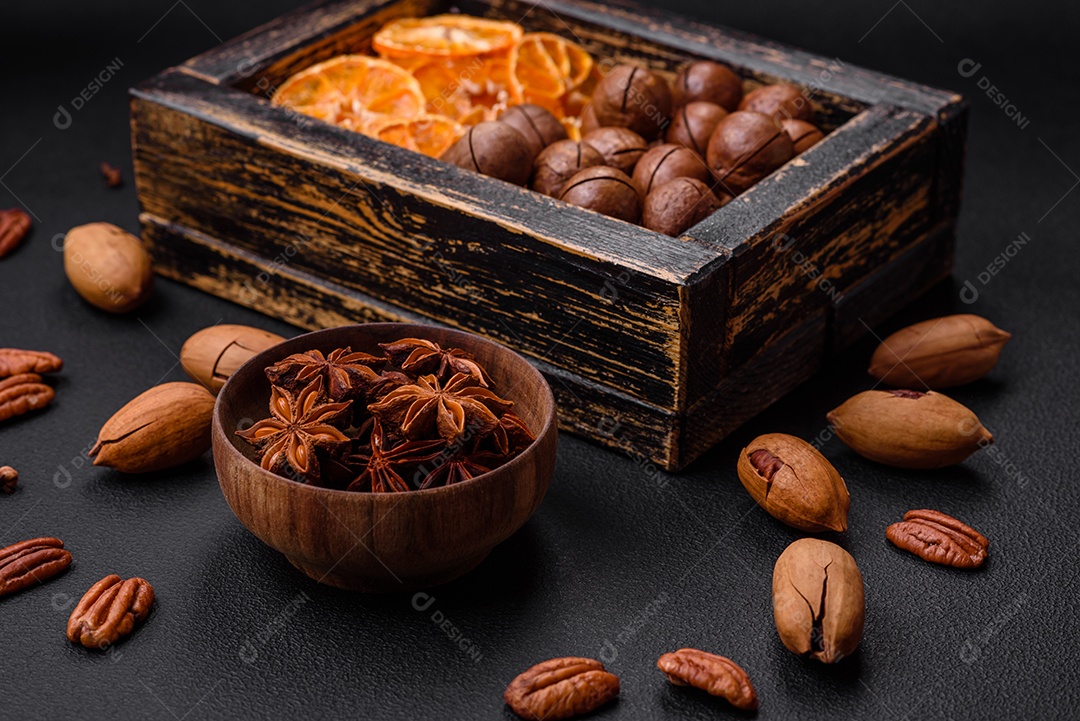 Nozes torradas e nozes de macadâmia, tangerina seca, frutos secos sobre um fundo escuro de concreto