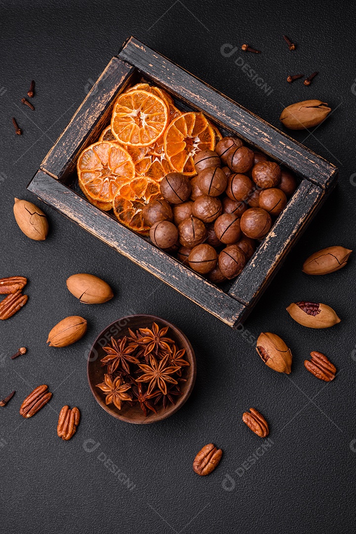 Nozes torradas e nozes de macadâmia, tangerina seca, frutos secos sobre um fundo escuro de concreto