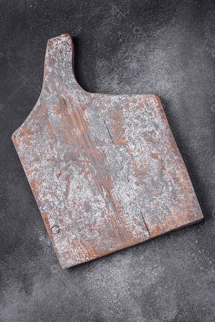 Tábua de corte de madeira vazia com rachaduras e arranhões localizados em um fundo escuro de concreto