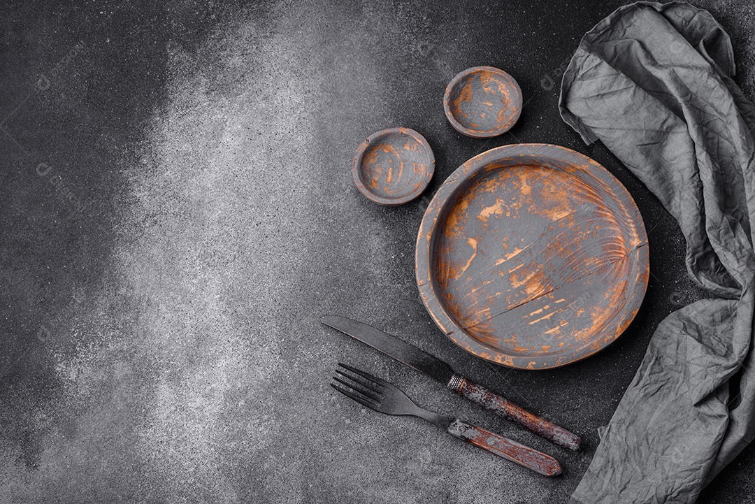 Prato de madeira vazio, faca, garfo e tábua de corte em fundo de concreto texturizado