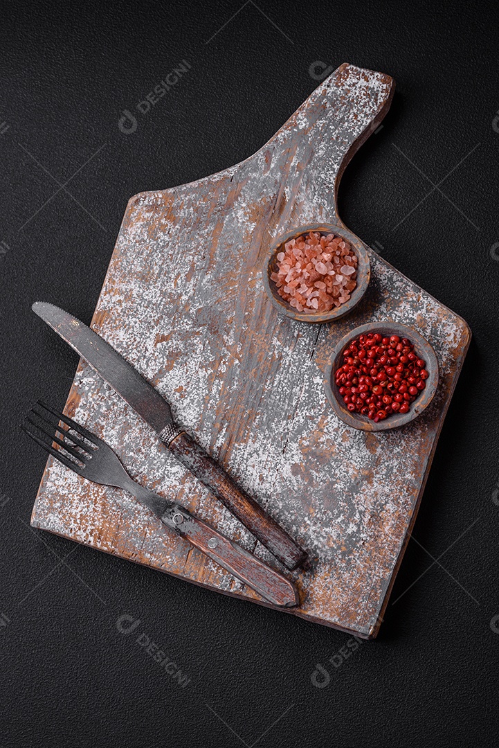 Faca garfo e tábua sal pimenta e outros ingredientes localizados em um fundo de concreto texturizado