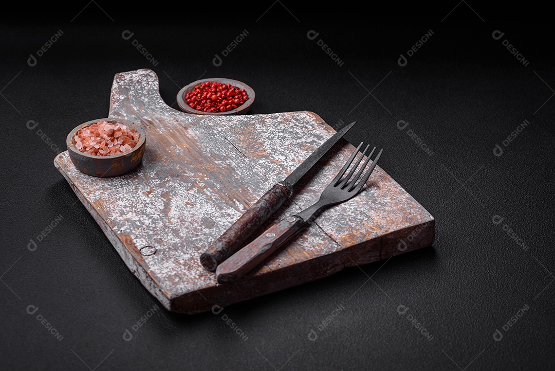 Faca garfo e tábua sal pimenta e outros ingredientes localizados em um fundo de concreto texturizado