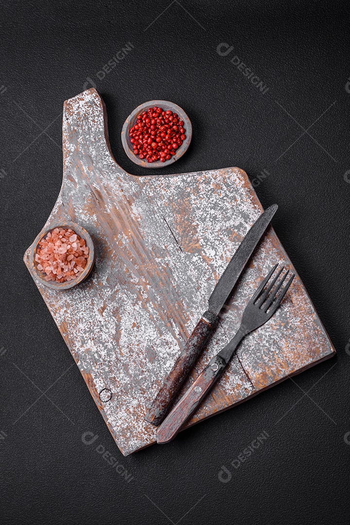 Faca garfo e tábua sal pimenta e outros ingredientes localizados em um fundo de concreto texturizado