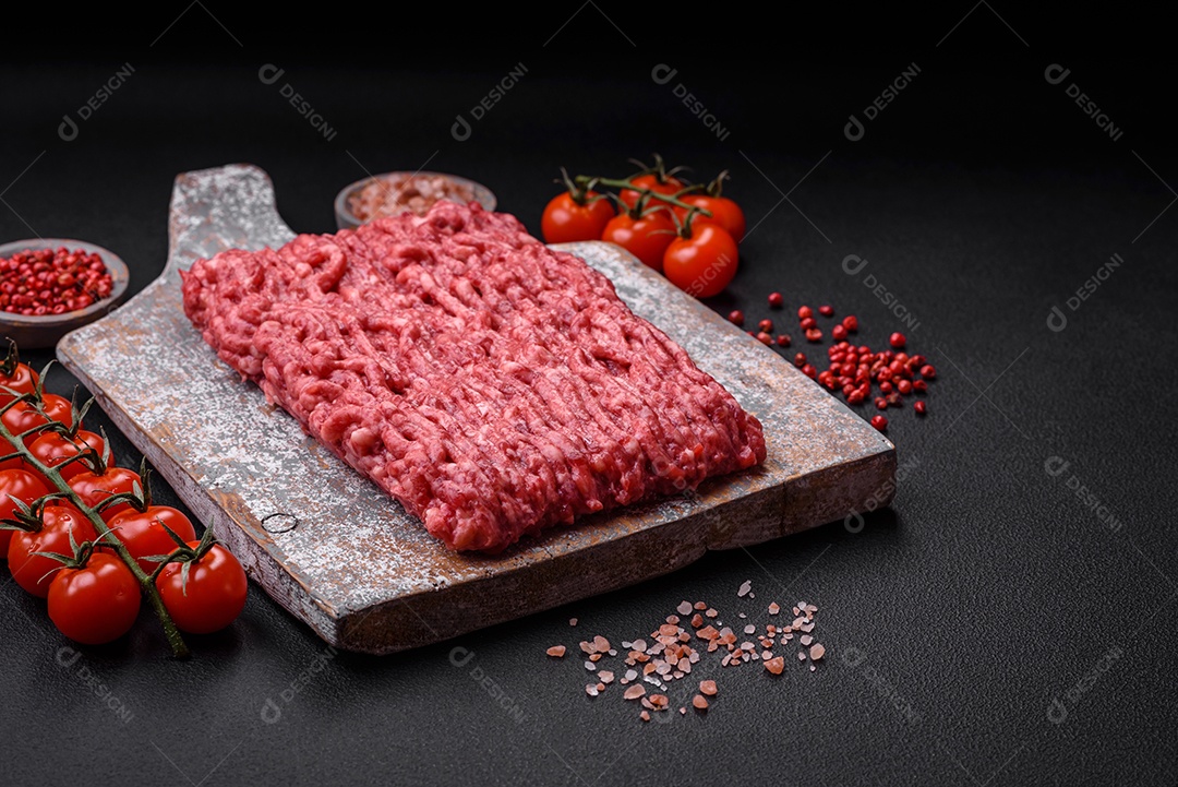 Carne moída crua ou carne de porco em uma tábua de madeira com especiarias e sal sobre um fundo escuro de concreto