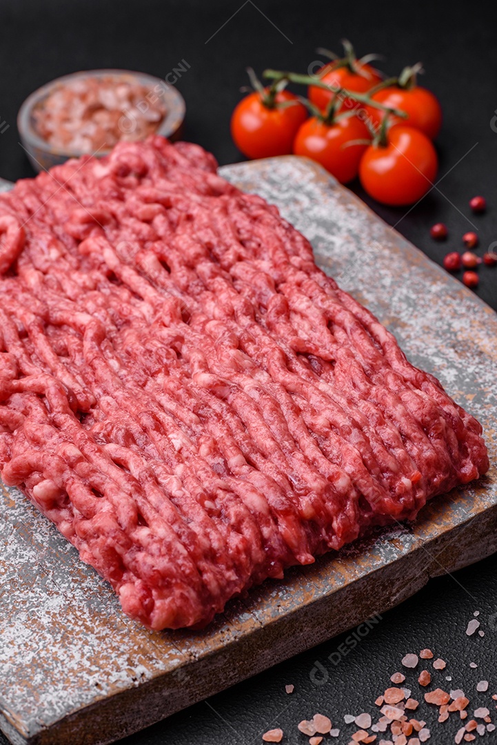 Carne moída crua ou carne de porco em uma tábua de madeira com especiarias e sal sobre um fundo escuro de concreto