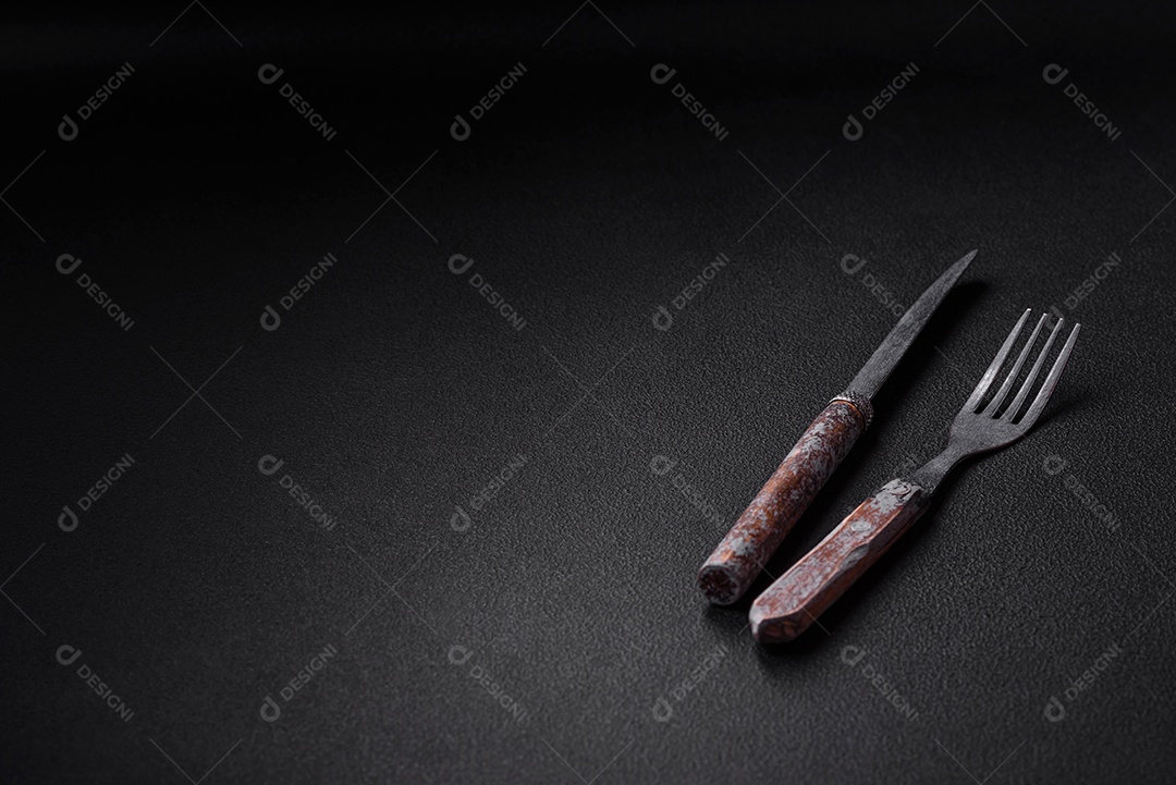 Faca, garfo e tábua, sal, pimenta e outros ingredientes localizados em um fundo de concreto texturizado