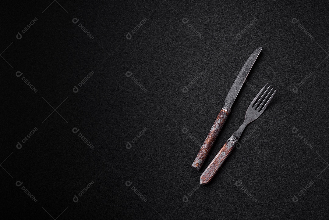 Faca, garfo e tábua, sal, pimenta e outros ingredientes localizados em um fundo de concreto texturizado