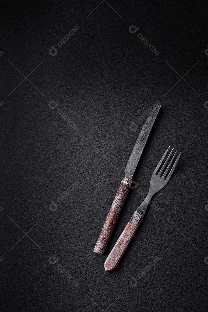 Faca, garfo e tábua, sal, pimenta e outros ingredientes localizados em um fundo de concreto texturizado