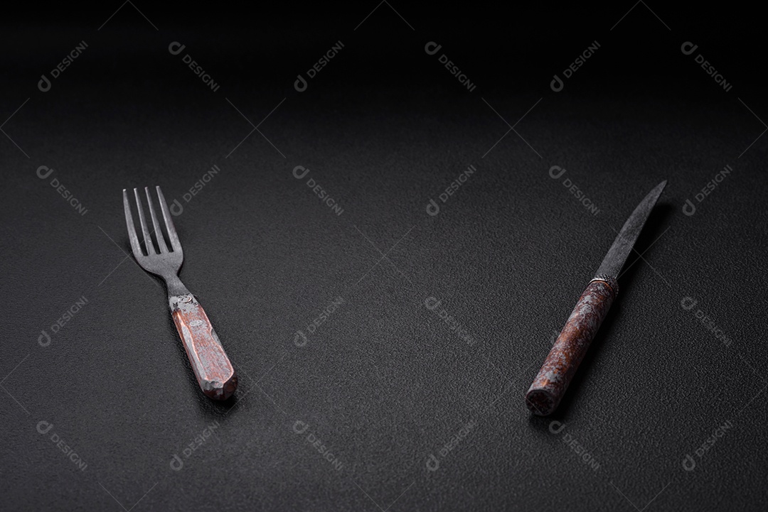 Faca, garfo e tábua, sal, pimenta e outros ingredientes localizados em um fundo de concreto texturizado