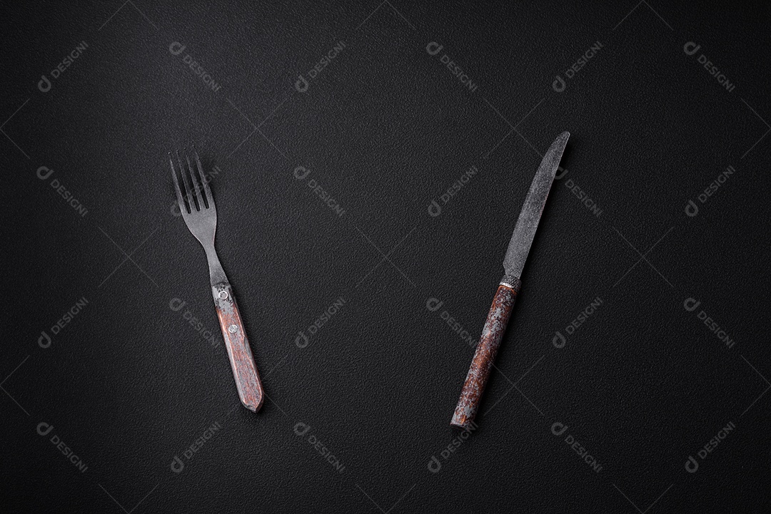 Faca, garfo e tábua, sal, pimenta e outros ingredientes localizados em um fundo de concreto texturizado