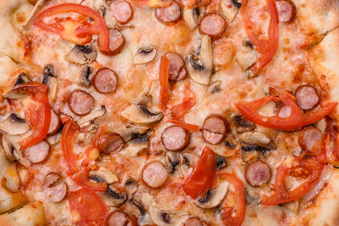 Pizza bávara com enchidos, tomates, queijo, sal e especiarias sobre um fundo escuro de concreto