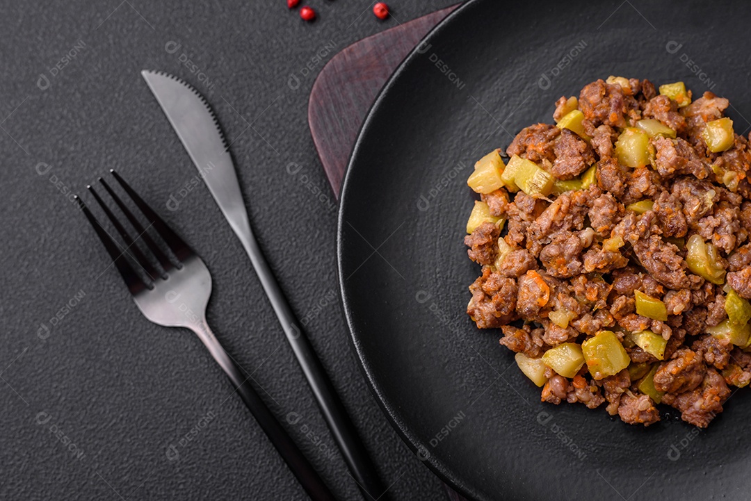 Saboroso prato composto por abobrinha, carne bovina, cogumelos, cebola e alho com sal e especiarias sobre um fundo escuro de concreto
