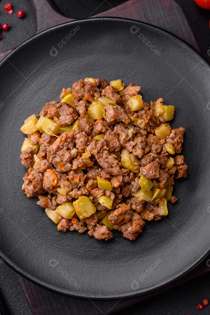 Saboroso prato composto por abobrinha, carne bovina, cogumelos, cebola e alho com sal e especiarias sobre um fundo escuro de concreto