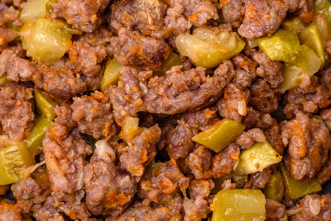 Saboroso prato composto por abobrinha, carne bovina, cogumelos, cebola e alho com sal e especiarias sobre um fundo escuro de concreto