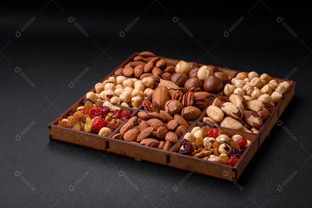 Mistura de nozes de macadâmia torradas, castanhas de caju, nozes, amêndoas, passas e frutos secos sobre um fundo escuro de concreto