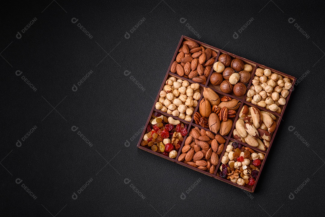 Mistura de nozes de macadâmia torradas, castanhas de caju, nozes, amêndoas, passas e frutos secos sobre um fundo escuro de concreto