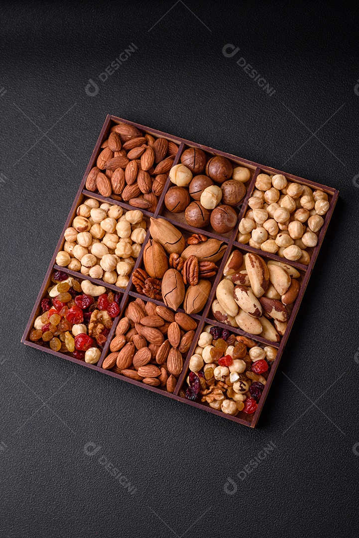 Mistura de nozes de macadâmia torradas, castanhas de caju, nozes, amêndoas, passas e frutos secos sobre um fundo escuro de concreto