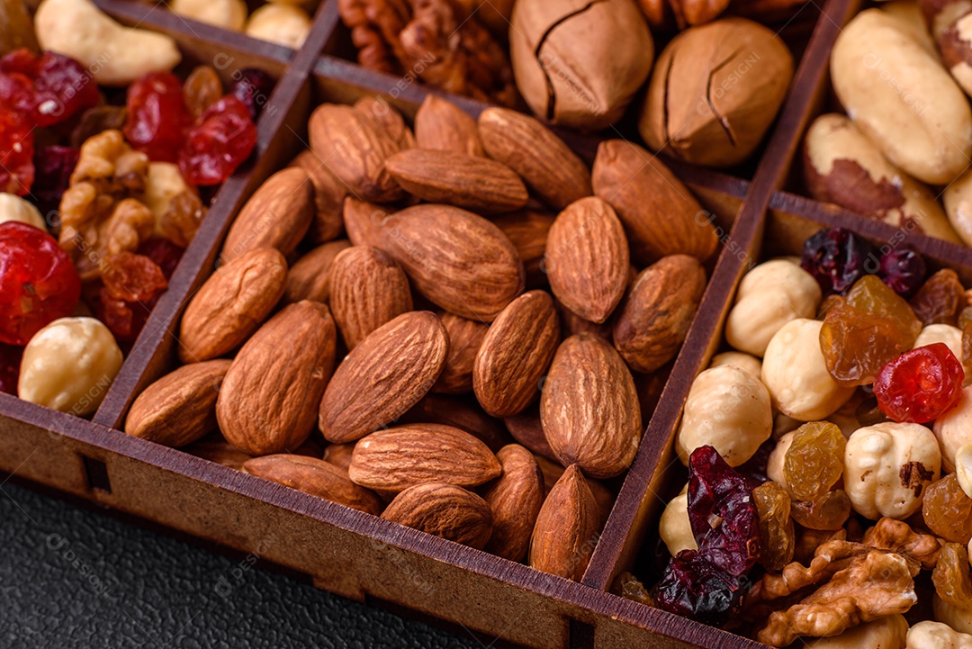 Mistura de nozes de macadâmia torradas, castanhas de caju, nozes, amêndoas, passas e frutos secos sobre um fundo escuro de concreto