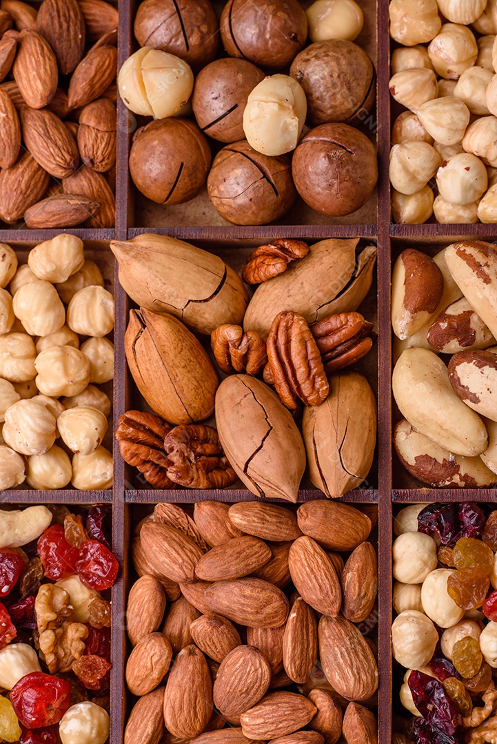 Mistura de nozes de macadâmia torradas, castanhas de caju, nozes, amêndoas, passas e frutos secos sobre um fundo escuro de concreto