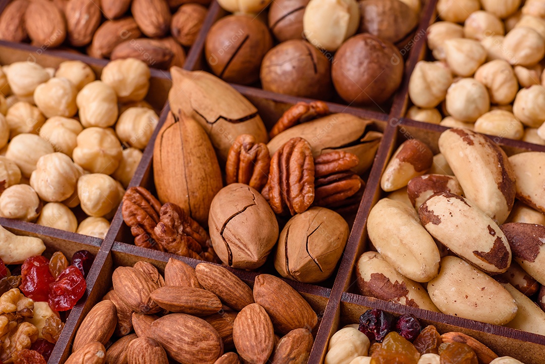 Mistura de nozes de macadâmia torradas, castanhas de caju, nozes, amêndoas, passas e frutos secos sobre um fundo escuro de concreto