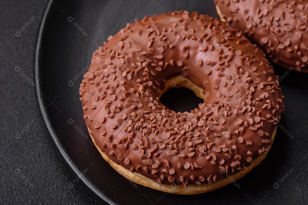 Delicioso donut com cobertura de chocolate polvilhado com pedaços de chocolate sobre um fundo escuro de concreto