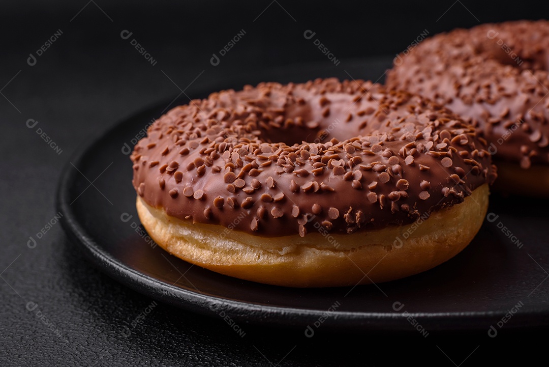 Delicioso donut com cobertura de chocolate polvilhado com pedaços de chocolate sobre um fundo escuro de concreto