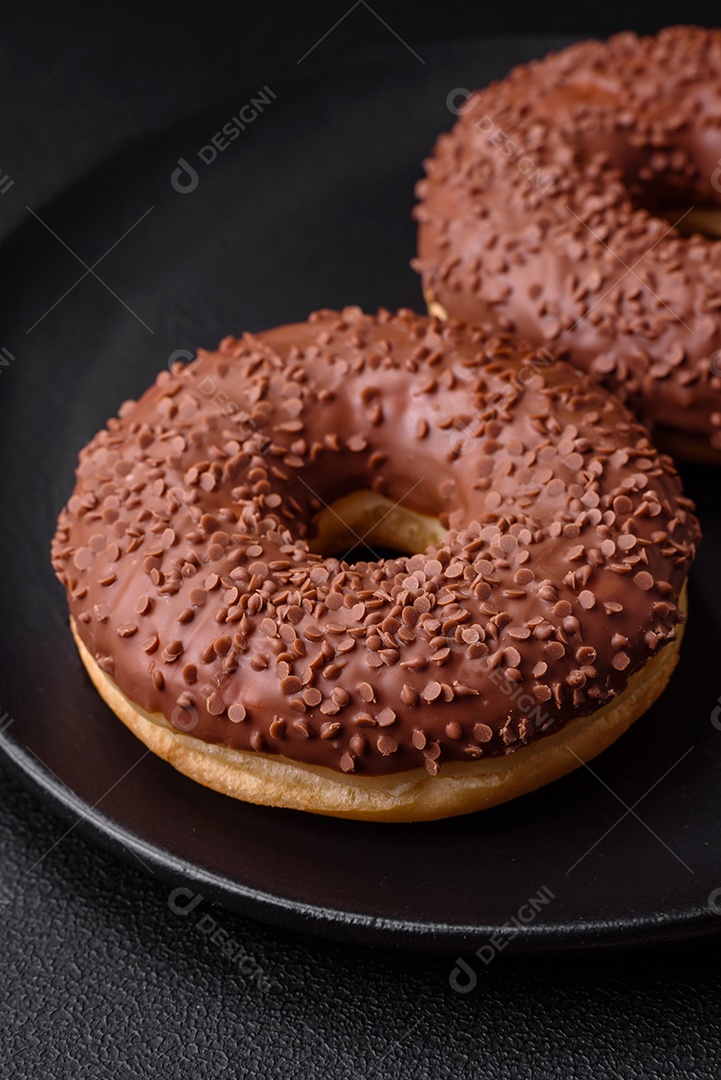 Delicioso donut com cobertura de chocolate polvilhado com pedaços de chocolate sobre um fundo escuro de concreto