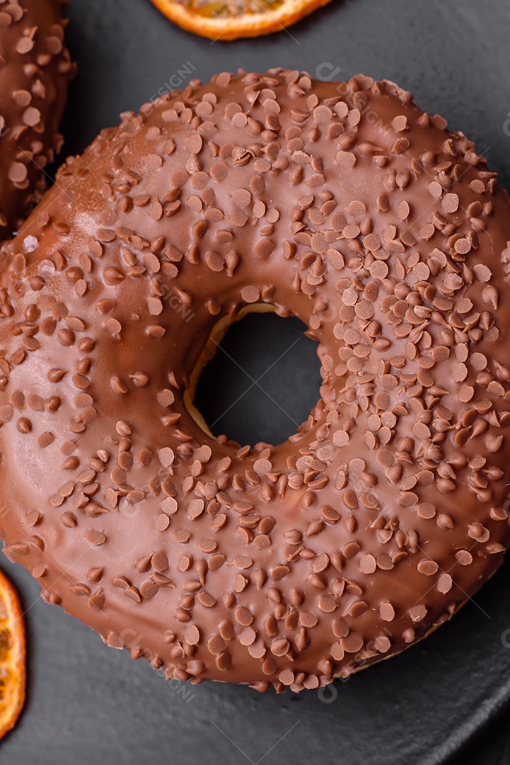 Delicioso donut com cobertura de chocolate polvilhado com pedaços de chocolate sobre um fundo escuro de concreto
