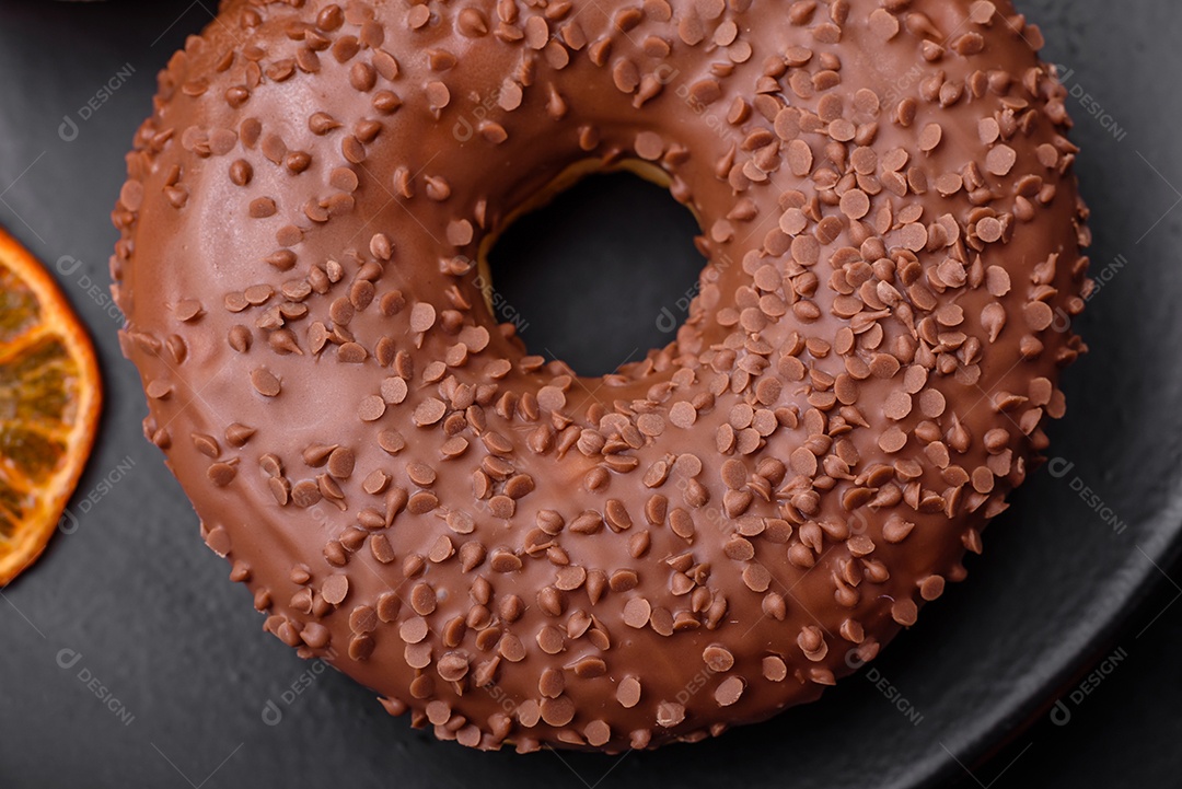 Delicioso donut com cobertura de chocolate polvilhado com pedaços de chocolate sobre um fundo escuro de concreto