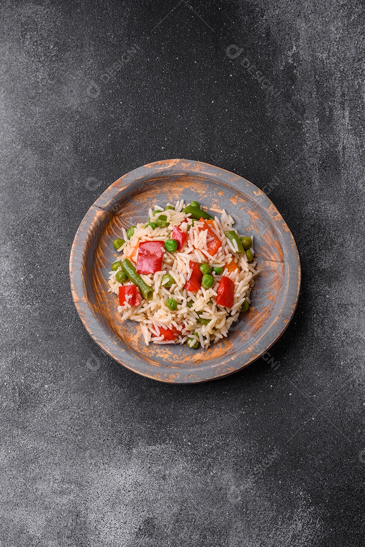 Delicioso arroz cozido com pimentão, ervilha, feijão de espargos e cenoura sobre um fundo de concreto texturizado