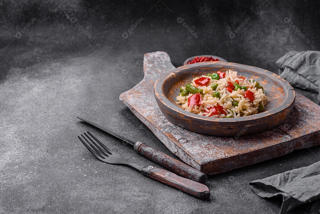 Delicioso arroz cozido com pimentão, ervilha, feijão de espargos e cenoura sobre um fundo de concreto texturizado