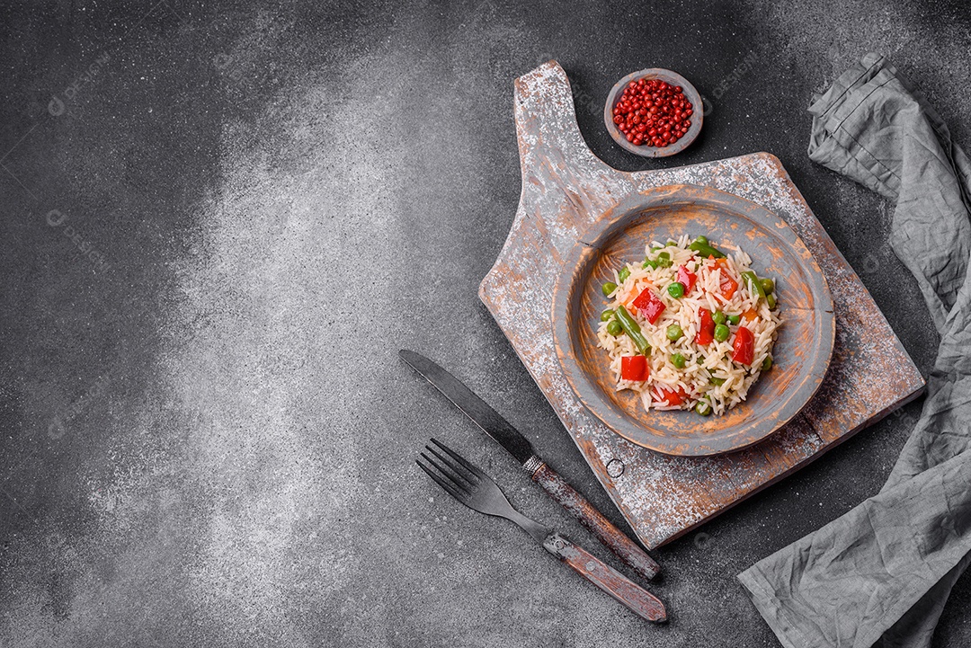 Delicioso arroz cozido com pimentão, ervilha, feijão de espargos e cenoura sobre um fundo de concreto texturizado