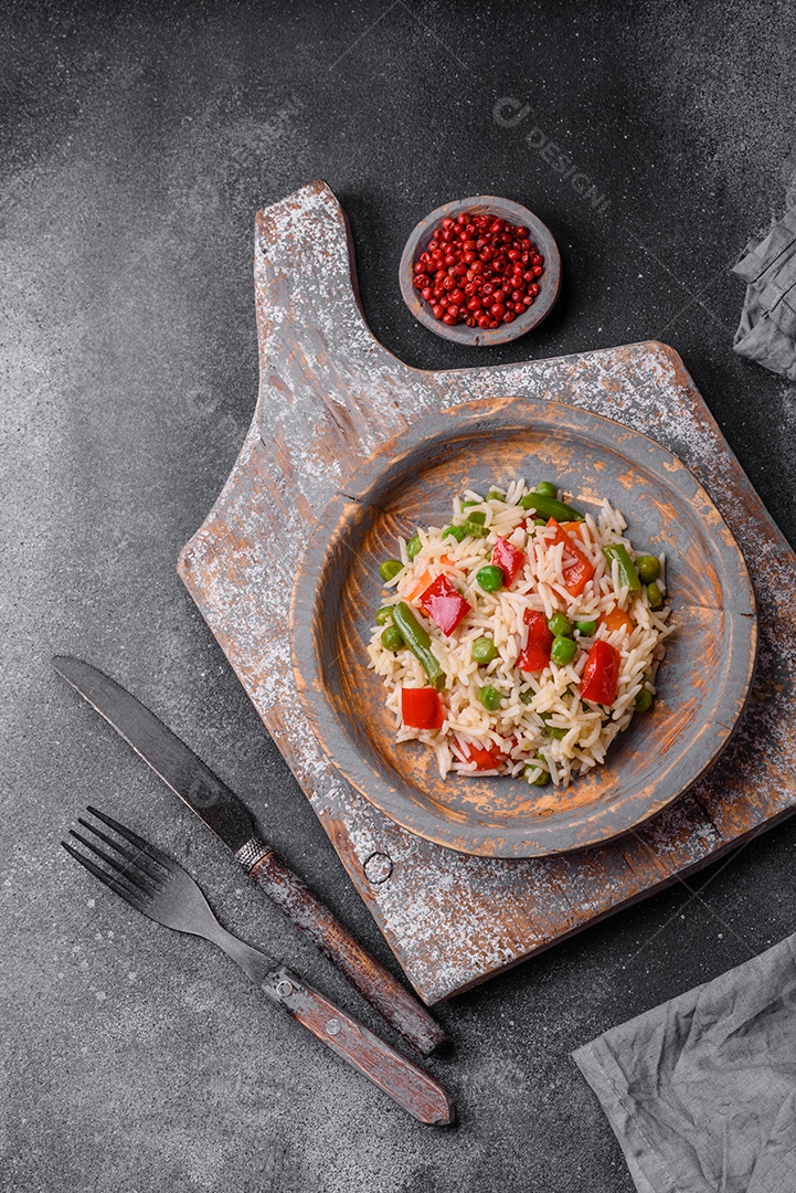 Delicioso arroz cozido com pimentão, ervilha, feijão de espargos e cenoura sobre um fundo de concreto texturizado