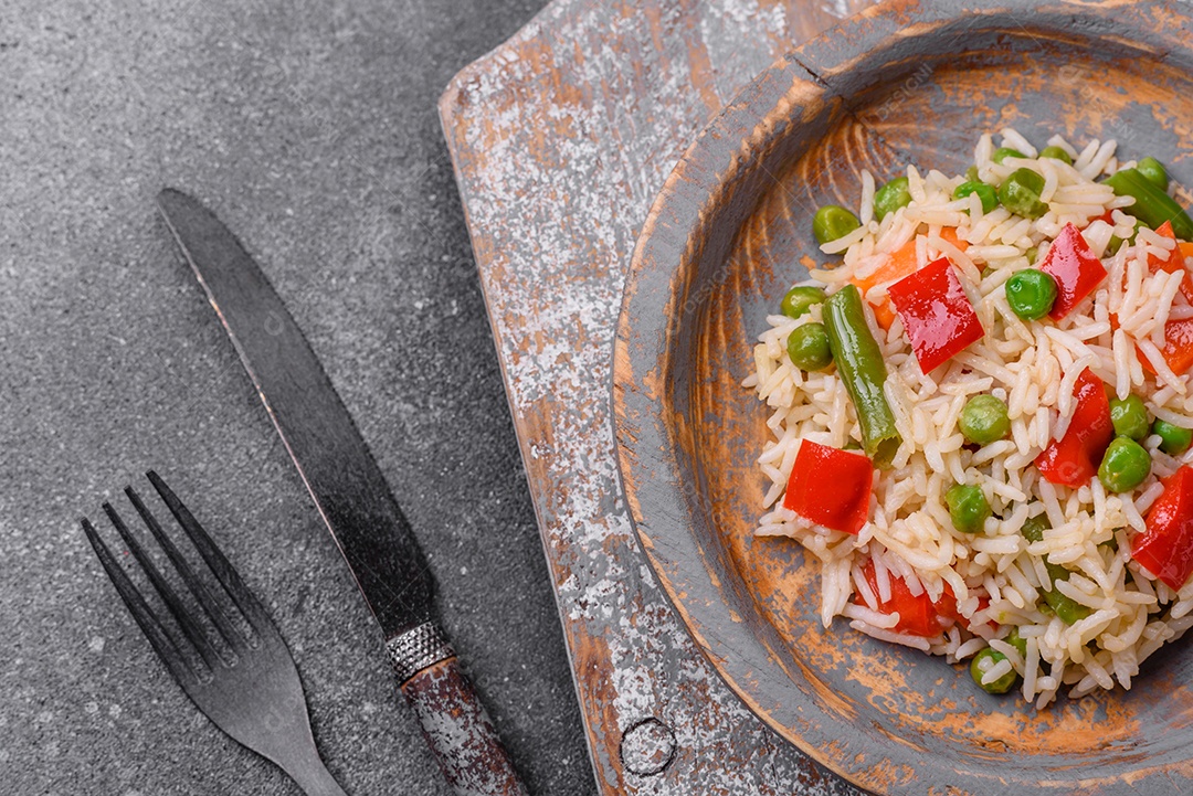 Delicioso arroz cozido com pimentão, ervilha, feijão de espargos e cenoura sobre um fundo de concreto texturizado