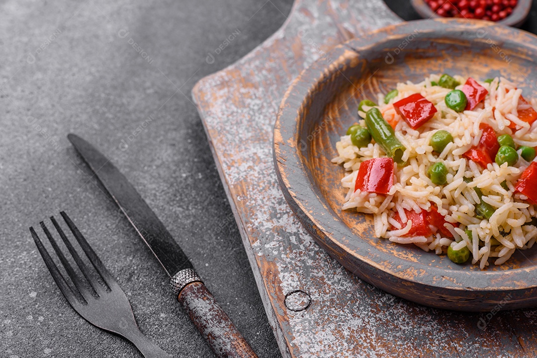 Delicioso arroz cozido com pimentão, ervilha, feijão de espargos e cenoura sobre um fundo de concreto texturizado